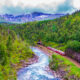 a train passing along Norway with mountain and river