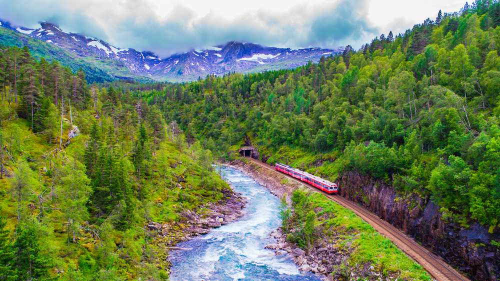 a scenic railway journey in Noway with mountains, river, an train coming out of a tunnel 