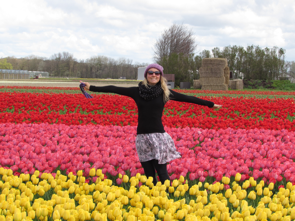 A woman poses in a field of flowers in a skirt and long sleeve shirt: it must be cooler, say March, because the tulips are blooming but she wears a scarf still! 