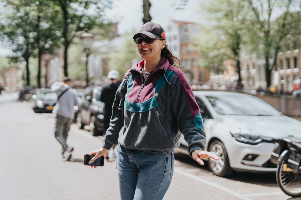 A woman knows what to wear to Amsterdam in spring, as she channels a sporty outdoors look in a zip up fleece, ball cap and jeans. 