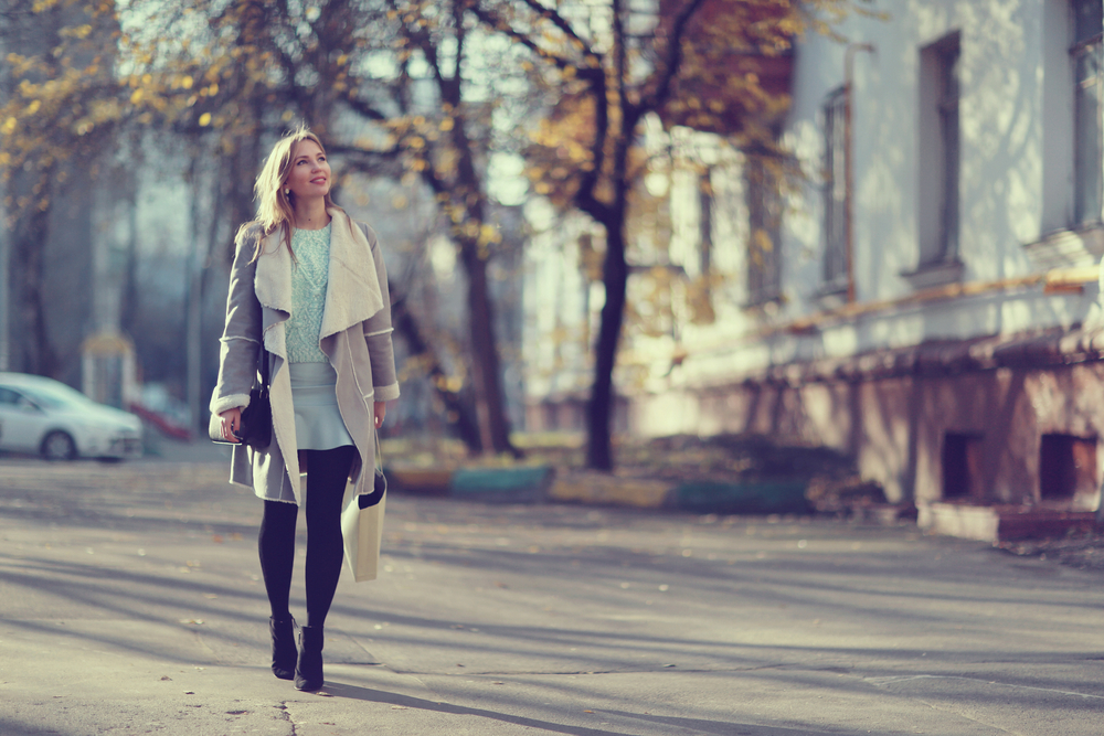 A woman explores the city not worrying about what to wear in New York City in winter, as she is warm and stylish in her skirt, tights, boots, jacket and sweater. 