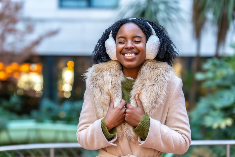 A woman knows exactly what to wear in New York City in winter, as she is bundled up with a faux fur jacket, a sweater, and ear warmers! 