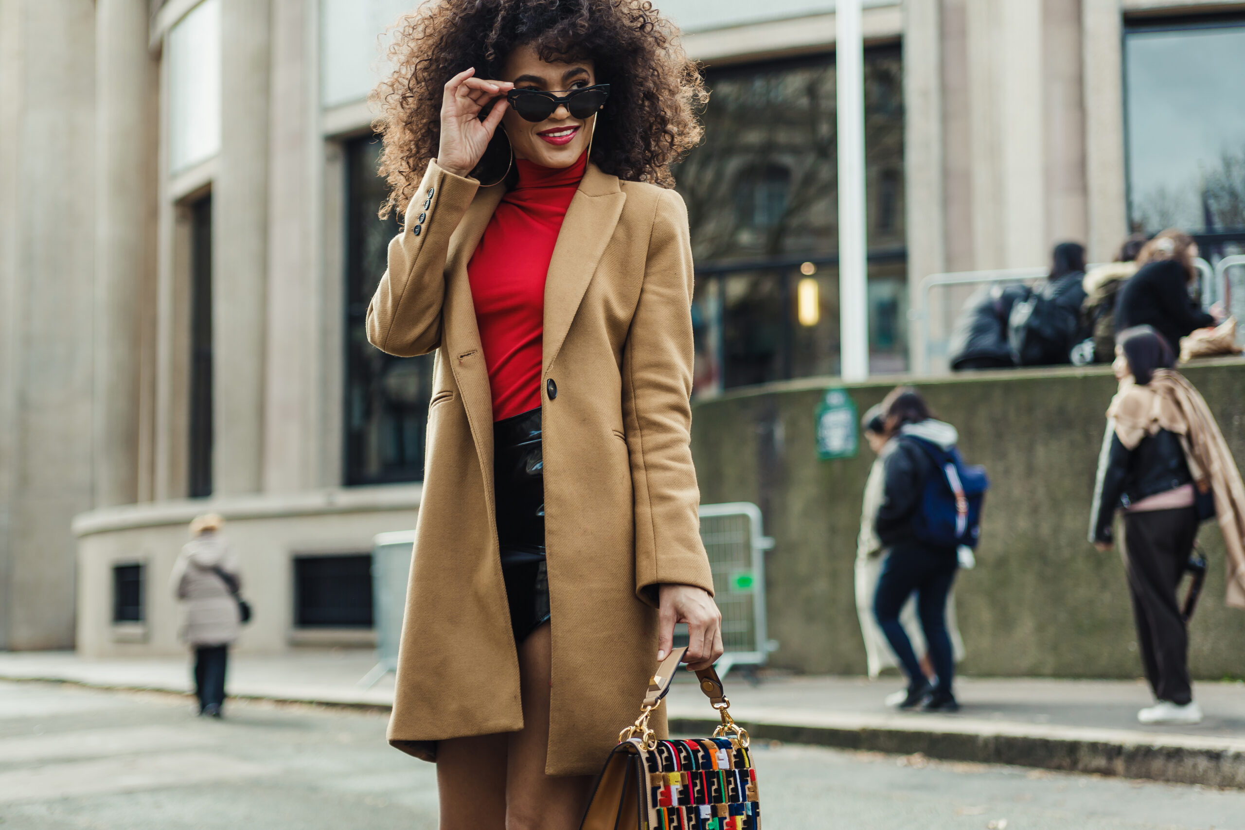 A woman looks over her sunglasses as she crosses the street in Paris while wearing a wool sweater, a red turtleneck, a leather skirt and tights. 