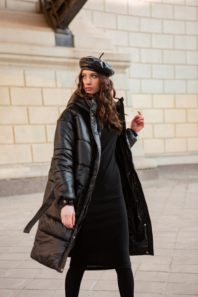 A woman walks down the street in a knit dress, a leather puffer jacket and a leather beret. 