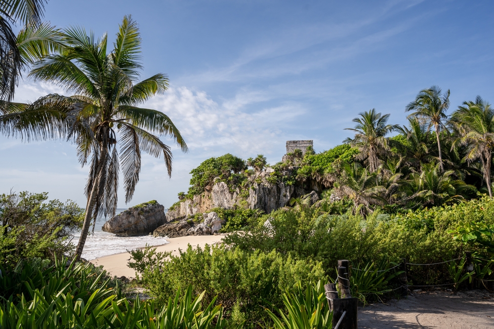 ruins of "Tulum" in Mexico on the top of a hills surrounded by trees and a beach. 